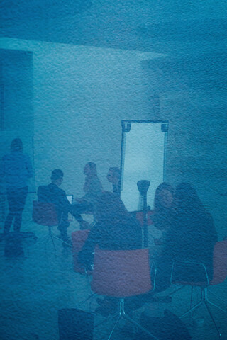 Ein moderner Saal mit sitzenden Personen und Flipcharts.