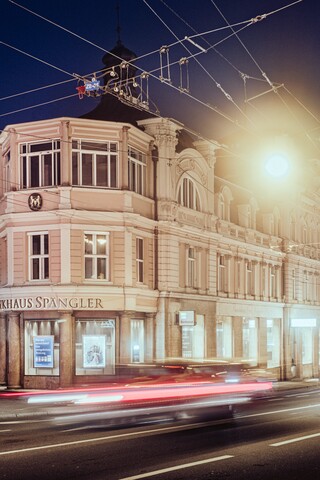 Schlossähnliches historisches Gebäude in der Dunkelheit hinter vorbeifahrenden Autos und Stromleitungen.