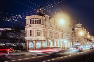 Schlossähnliches historisches Gebäude in der Dunkelheit hinter vorbeifahrenden Autos und Stromleitungen.