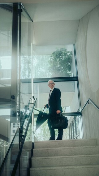 Person in Business-Kleidung steht auf einer Treppe in einem modernen Treppenhaus und blickt in die Kamera.