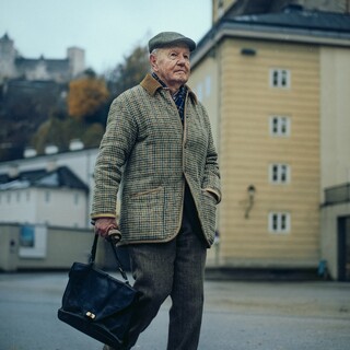 Ein älterer Herr mit Aktentasche spaziert durch eine verregnete Stadt.