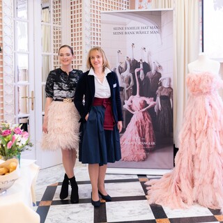 Zwei Damen und eine Schaufensterpuppe in eleganter Kleidung stehen vor einem Rollup.