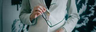 Frau mit Blazer hält eine schwarze Brille in der Hand