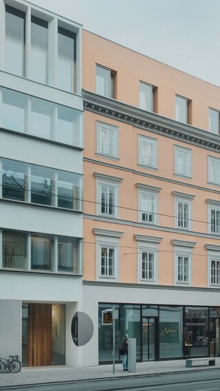 Außenansicht eines Gebäudes mit großen Glasflächen und heller Fassade im Straßenraum.