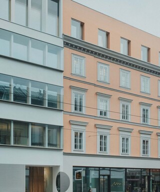 Außenansicht eines Gebäudes mit großen Glasflächen und heller Fassade im Straßenraum.