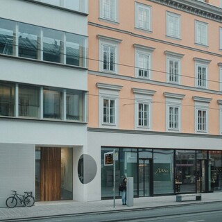 Außenansicht eines Gebäudes mit großen Glasflächen und heller Fassade im Straßenraum.