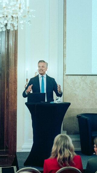 Dr. Werner Zenz hält eine Rede vor dem Publikum im Rahmen des Forums Familienunternehmen 2024. In der linken oberen Ecke ist ein Kronleuchter zu sehen, im rechten Teil des Bildes eine Leinwand. 