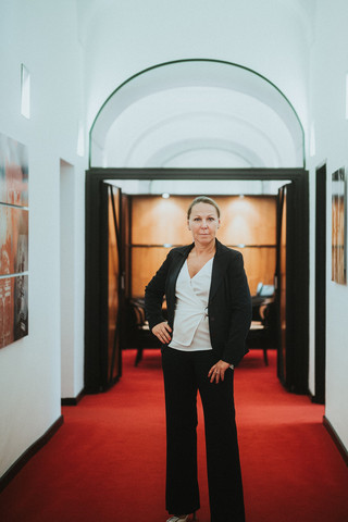 Eine Dame in Geschäftskleidung steht in einem Gang mit rotem Teppich.