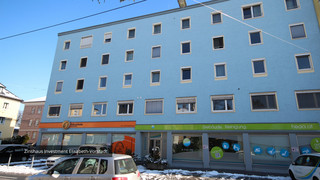 Einfaches Gebäude mit blauer Fassade von der Nähe mit vielen weißen Fenstern. Im Erdgeschoss sind die "Fahrschule Zaunschirm" und "Gebäude Reinigung" beheimatet.