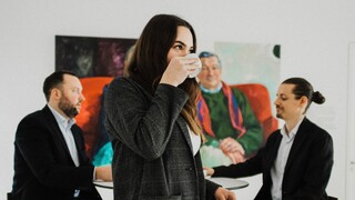 Eine Frau in schwarzem Kostüm steht in einem Raum und trinkt Kaffee.