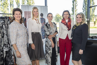 Fünf schick gekleidete Frauen lächeln.