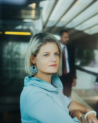 Eine Dame in Geschäftskleidung blickt in einem modernen Gebäude in die Ferne.