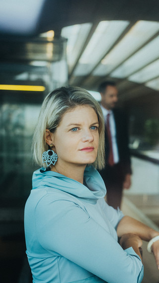 Eine Dame in Geschäftskleidung blickt in einem modernen Gebäude in die Ferne.