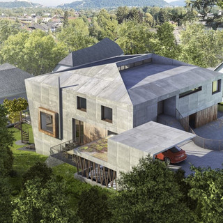 Blick von oben auf eine moderne Immobilie von außen in grauer Farbe. Das Wohnhaus ist in eine grüne Naturlandschaft eingebettet