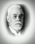 Schwarz-weißes Portraitfoto von einem älteren Herren mit vermutlich grauen Haaren und einem Bart, er trägt eine Brille. 