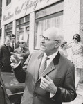 Schwarz-weiß-Bild, auf dem im Vordergrund ein älterer Herr mit gräulichen Haare und Brille, einen Anzug tragend, zu sehen ist. Im Hintergrund sind weitere Menschen - alle stehen vor einem Gebäude mit der Aufschrift "Bankhaus Carl Spängler".
