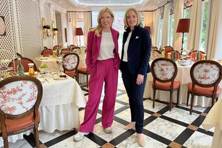 Zwei lächelnde Damen in eleganter Kleidung posieren zwischen edel gedeckten Tischen.