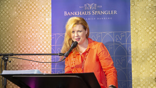 Sängerin spielt am Piano und singt. Sie trägt ein orangenes Kleid und hat blonde lange Haare.