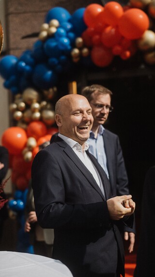 Herren in Geschäftskleidung stehen vor einem mit Luftballons geschmückten Portal.