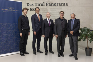 Fünf Herren in Geschäftskleidung posieren lächelnd vor einer Betonwand.