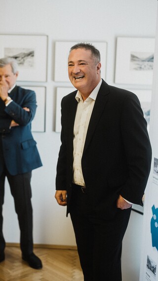 Ein lächelnder Herr in Anzug und ein weiterer in nachdenklicher Pose.