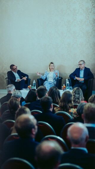 Publikum lauscht einer Podiumsdiskussion in einem historischen Saal.