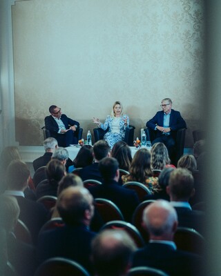 Publikum lauscht einer Podiumsdiskussion in einem historischen Saal.