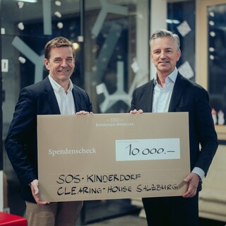 Zwei lächelnde Herren in Geschäftskleidung posieren mit einem Spendenscheck.