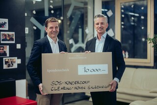 Zwei lächelnde Herren in Geschäftskleidung posieren mit einem Spendenscheck.