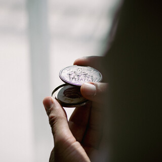 Eine geöffnete Schraubmünze liegt in der Hand einer Person. Ein Blick ins Innere wird freigegeben, die silberne Vorderseite zeigt ein detailgetreues Bild.