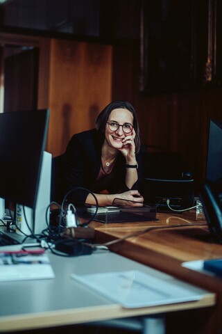 Eine lächelnde Dame lehnt auf einem Schreibtisch.