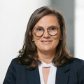 Lächelnde Dame in Geschäftskleidung stützt sich auf ein Geländer.
