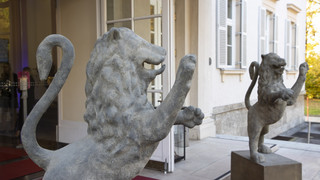 Zwei Löwen-Statuten aus Stein zieren den Eingang eines historischen Gebäudes.