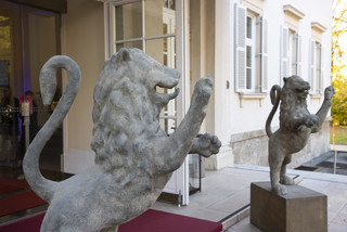 Zwei Löwen-Statuten aus Stein zieren den Eingang eines historischen Gebäudes.