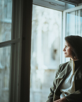 Eine Dame in Geschäftskleidung sitzt auf einer Fensterbank und blickt nach draußen.