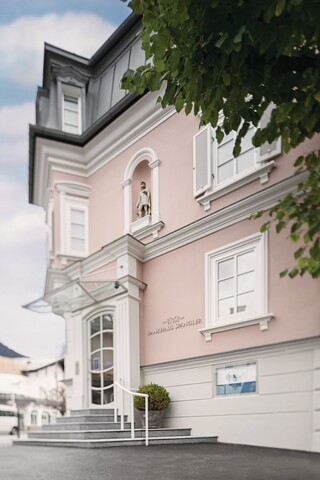 Fassade der Niederlassung Kitzbühel. Rosarotes historische Gebäude mit 3 Stockwerken und Treppenaufgang.