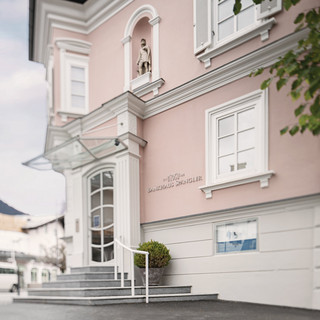 Fassade der Niederlassung Kitzbühel. Rosarotes historische Gebäude mit 3 Stockwerken und Treppenaufgang.