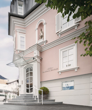 Fassade der Niederlassung Kitzbühel. Rosarotes historische Gebäude mit 3 Stockwerken und Treppenaufgang.