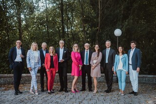 Eine Gruppe von Personen in Geschäftskleidung posiert lächelnd vor einem Wald.