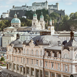 Stammhaus des Bankhaus Spängler in der Schwarzstraße 1 in 5020 Salzburg von außen. Die Fassade ist hellrosa, auffällig ist das Kuppeldach. Im Hintergrund sieht man die Festung Hohensalzburg sowie die Kuppeln des Salzburger Doms. 