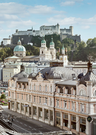 Stammhaus des Bankhaus Spängler in der Schwarzstraße 1 in 5020 Salzburg von außen. Die Fassade ist hellrosa, auffällig ist das Kuppeldach. Im Hintergrund sieht man die Festung Hohensalzburg sowie die Kuppeln des Salzburger Doms. 