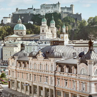 Stammhaus des Bankhaus Spängler in der Schwarzstraße 1 in 5020 Salzburg von außen. Die Fassade ist hellrosa, auffällig ist das Kuppeldach. Im Hintergrund sieht man die Festung Hohensalzburg sowie die Kuppeln des Salzburger Doms. 
