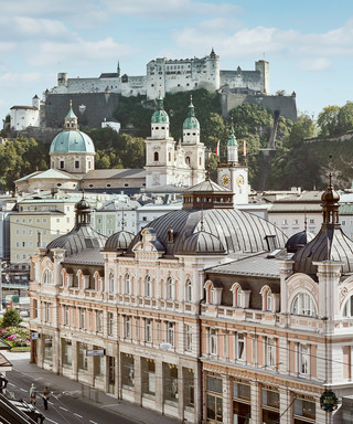 Stammhaus des Bankhaus Spängler in der Schwarzstraße 1 in 5020 Salzburg von außen. Die Fassade ist hellrosa, auffällig ist das Kuppeldach. Im Hintergrund sieht man die Festung Hohensalzburg sowie die Kuppeln des Salzburger Doms. 