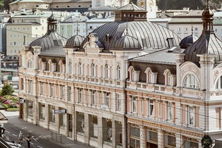 Stammhaus des Bankhaus Spängler in der Schwarzstraße 1 in 5020 Salzburg von außen. Die Fassade ist hellrosa, auffällig ist das Kuppeldach. Im Hintergrund sieht man die Festung Hohensalzburg sowie die Kuppeln des Salzburger Doms. 