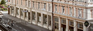 Stammhaus des Bankhaus Spängler in der Schwarzstraße 1 in 5020 Salzburg von außen. Die Fassade ist hellrosa, auffällig ist das Kuppeldach. Im Hintergrund sieht man die Festung Hohensalzburg sowie die Kuppeln des Salzburger Doms. 