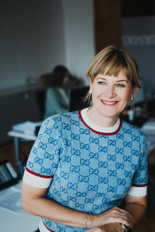 Eine lächelnde Dame in Pullover posiert in einem Büro.