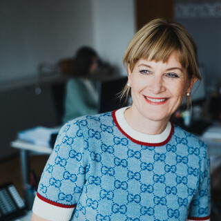 Eine lächelnde Dame in Pullover posiert in einem Büro.