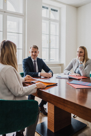 Drei Personen sitzen an einem Tisch und besprechen etwas.