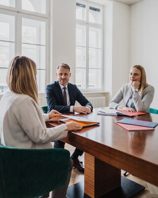 Drei Personen sitzen an einem Tisch und besprechen etwas.