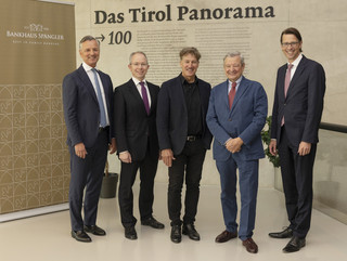 Fünf Männer in Anzügen lächeln in die Kamera. Sie stehen vor einer Wand mit der Aufschrift "Bankhaus Spängler" und "Das Tirol Panorama".